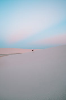 A lone individual in the vast Atins desert dunes at sunset, capturing a serene moment.