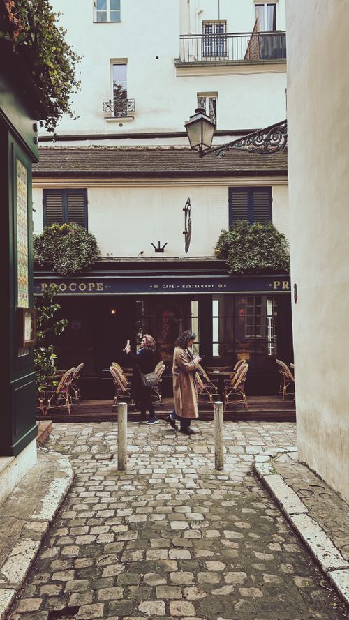 Free Discover the charming Procope café in Paris, France, offering a cozy outdoor seating area on a picturesque cobblestone street. Stock Photo