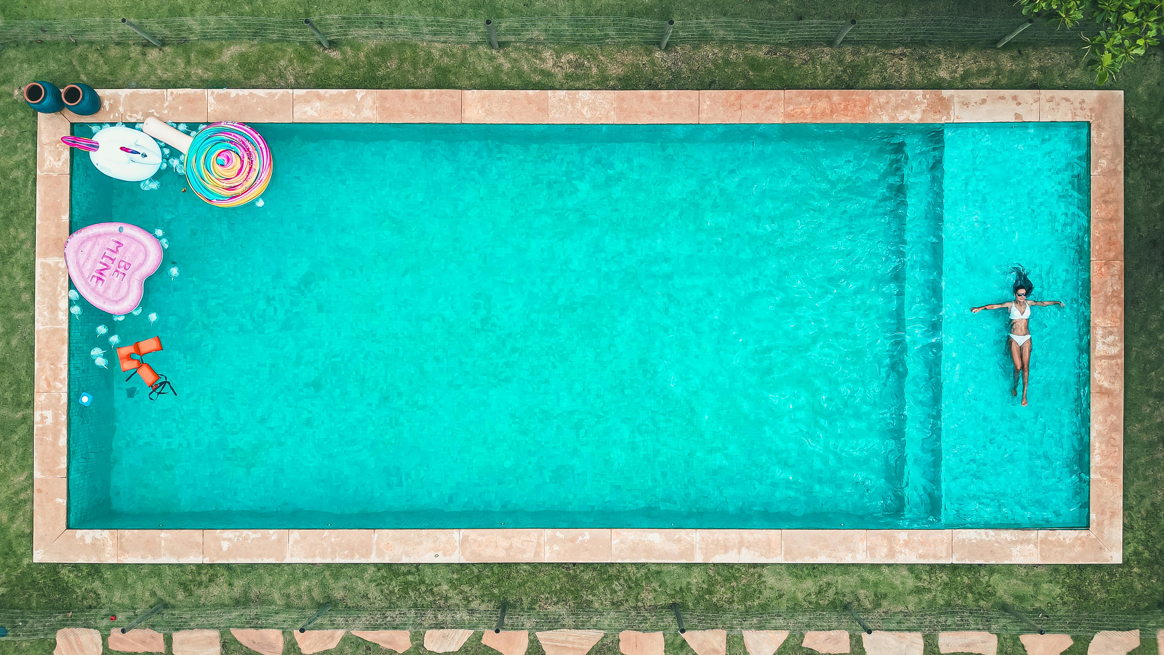 Top-down drone shot of a woman relaxing in a colorful pool with inflatables, perfect summer scene.