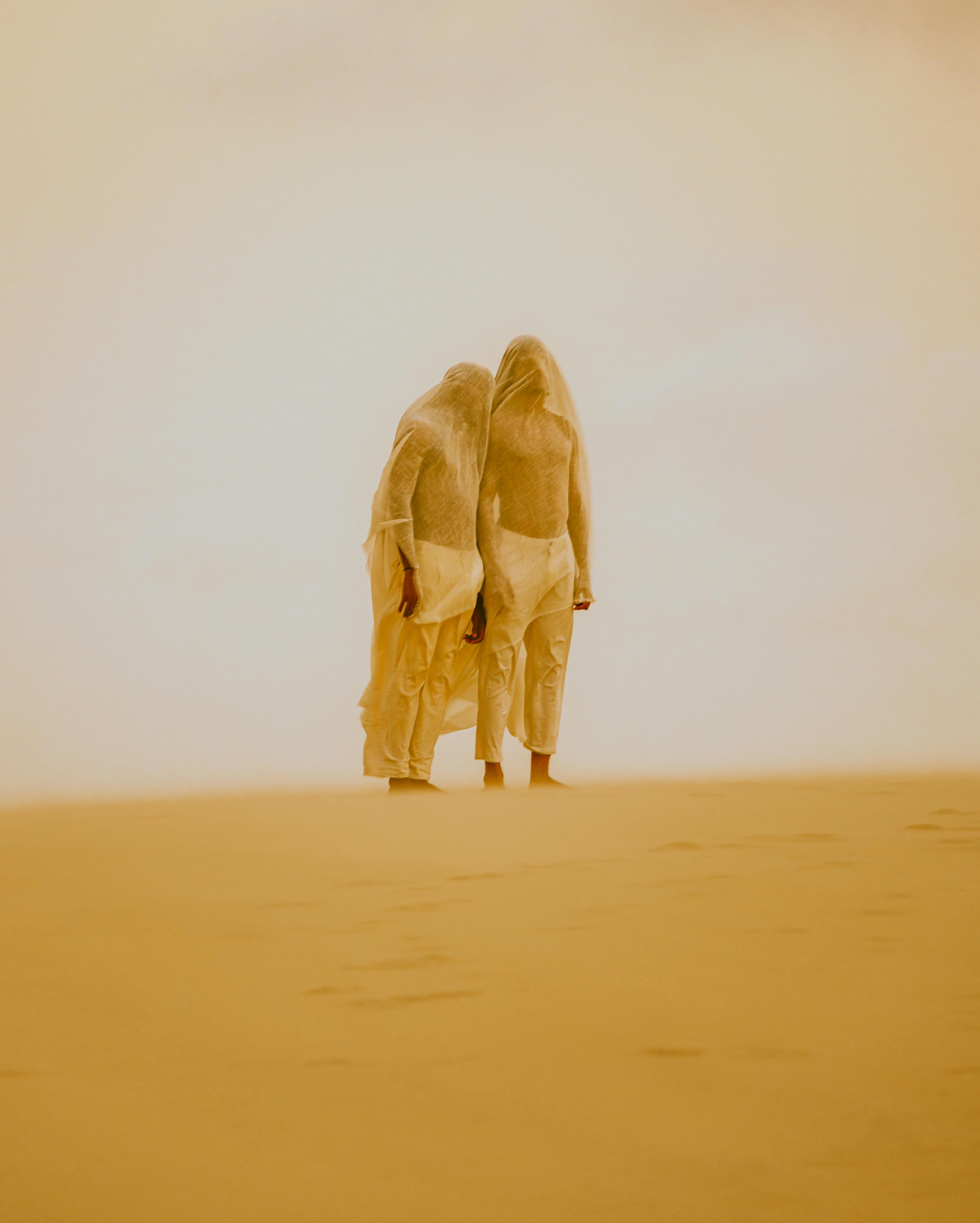 Two veiled figures stand in the sandy expanses of Atins, Brazil, evoking mystique and artistic expression.