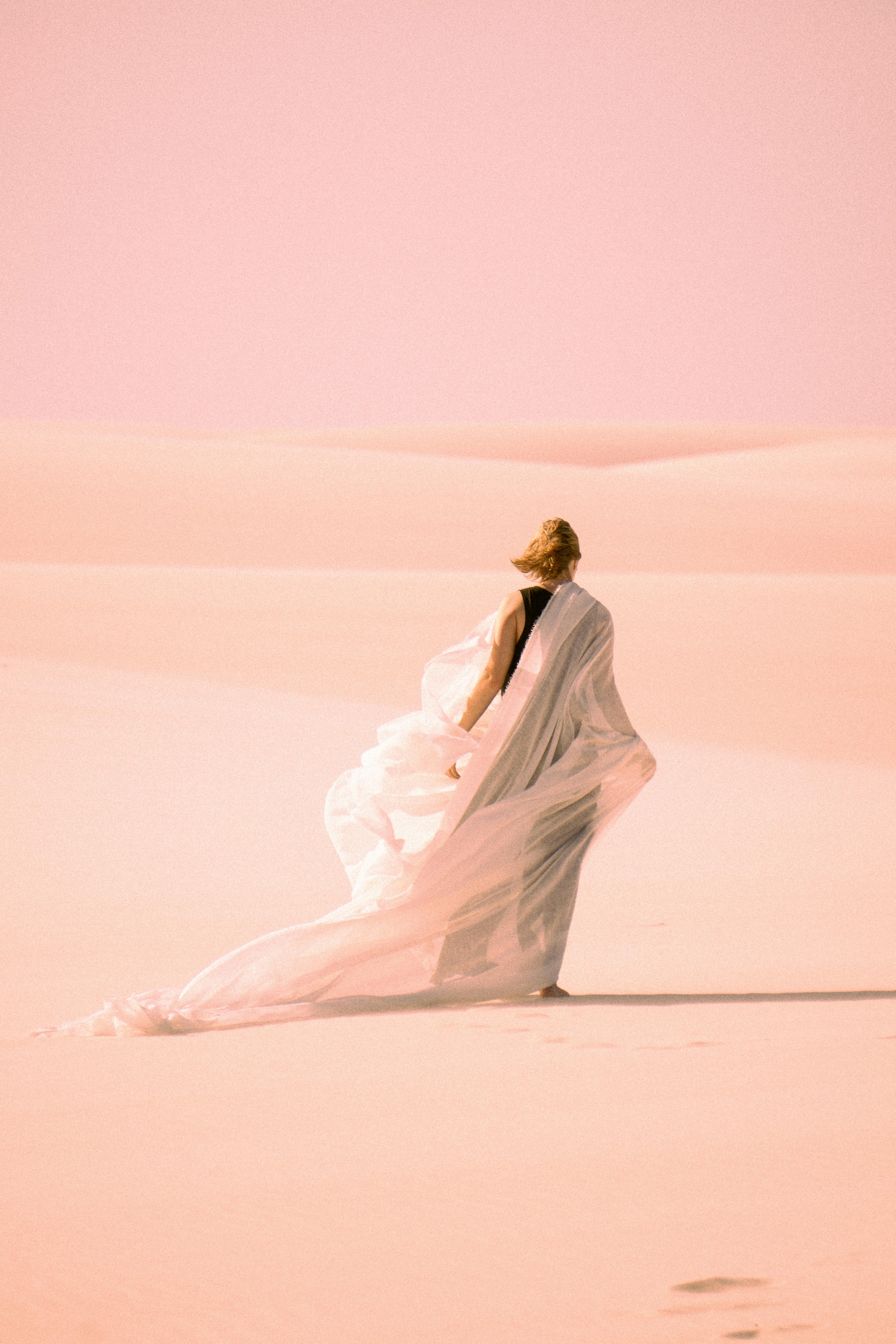 rear view of a woman wrapped in a white shawl standing on the sand dune