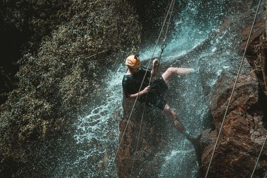 An adventurous person rappelling down a waterfall in a natural setting, showcasing outdoor excitement.