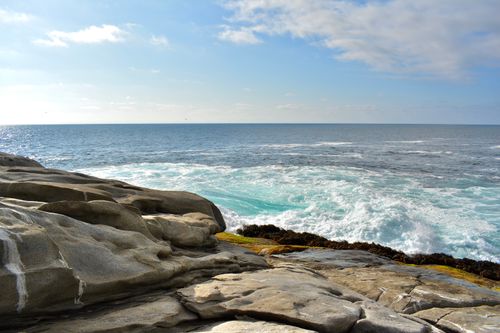 Free Breathtaking view of ocean waves crashing on rocky coastline under a bright blue sky. Stock Photo