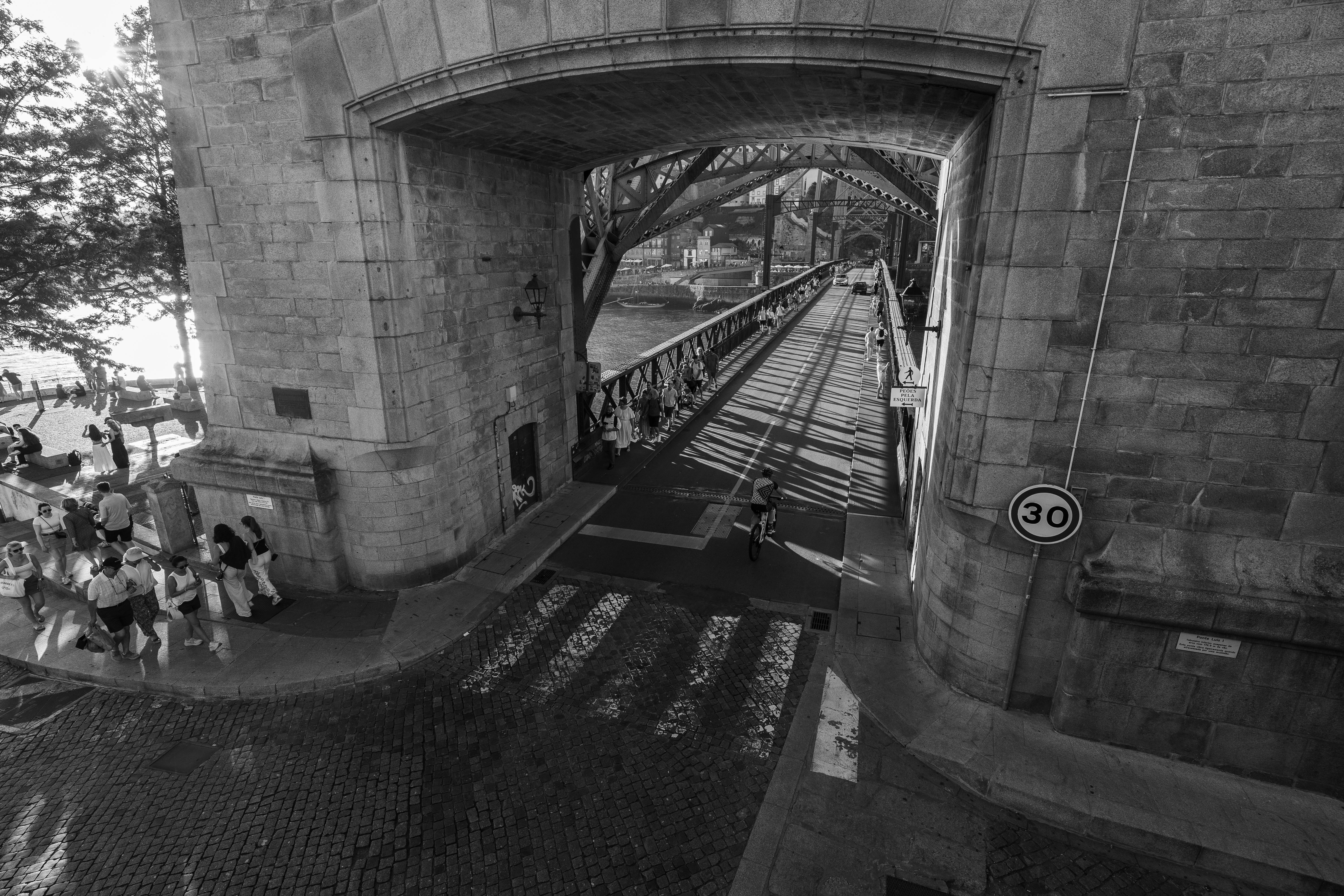 A black and white high-angle shot of pedestrians on the iconic Ponte de Dom Luís I bridge in Porto.