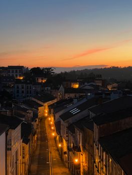 Aerial view of Santiago de Compostela at twilight with warm streetlights and a vivid sunset sky.