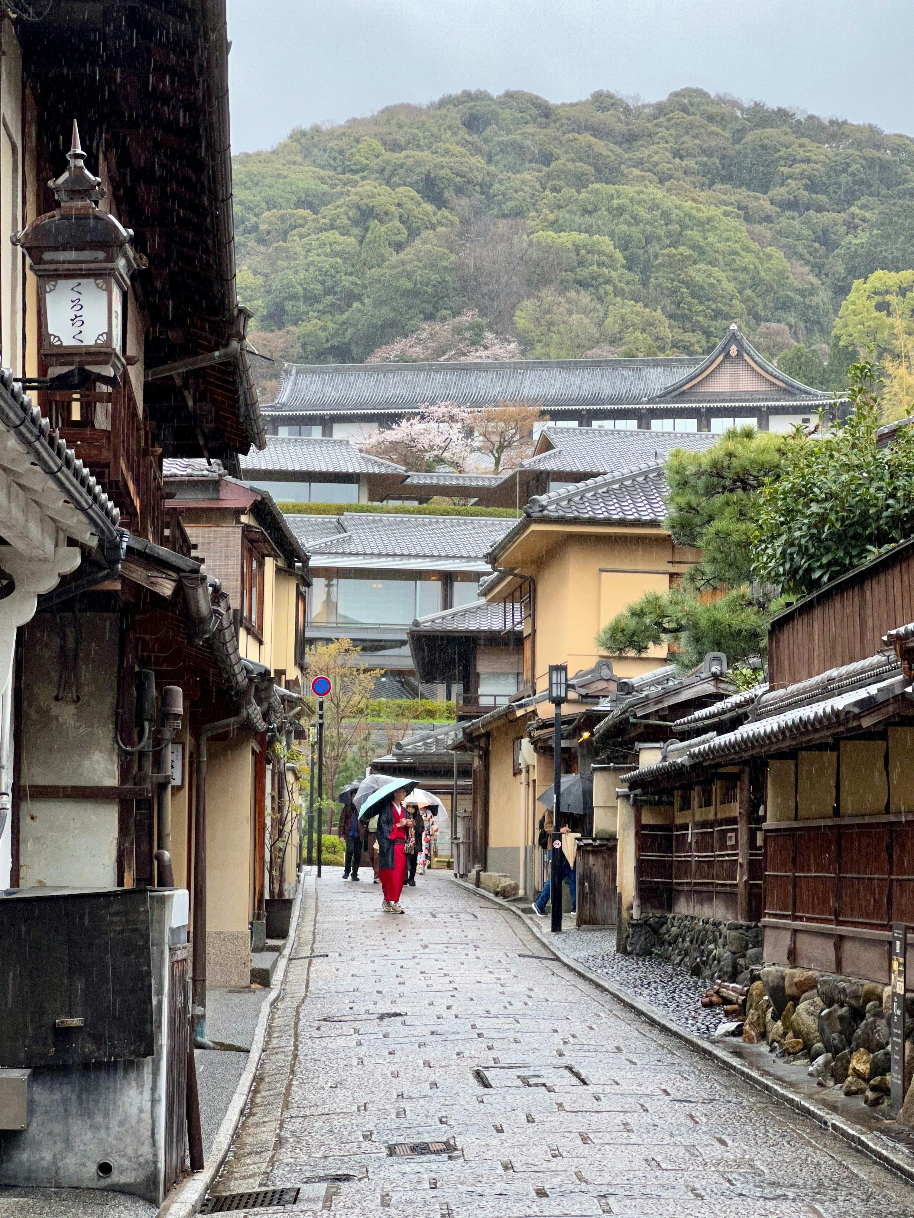 a woman walking down a narrow street in a kyoto city