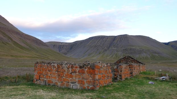 Abandoned red brick ruins set against a scenic Icelandic mountain landscape.