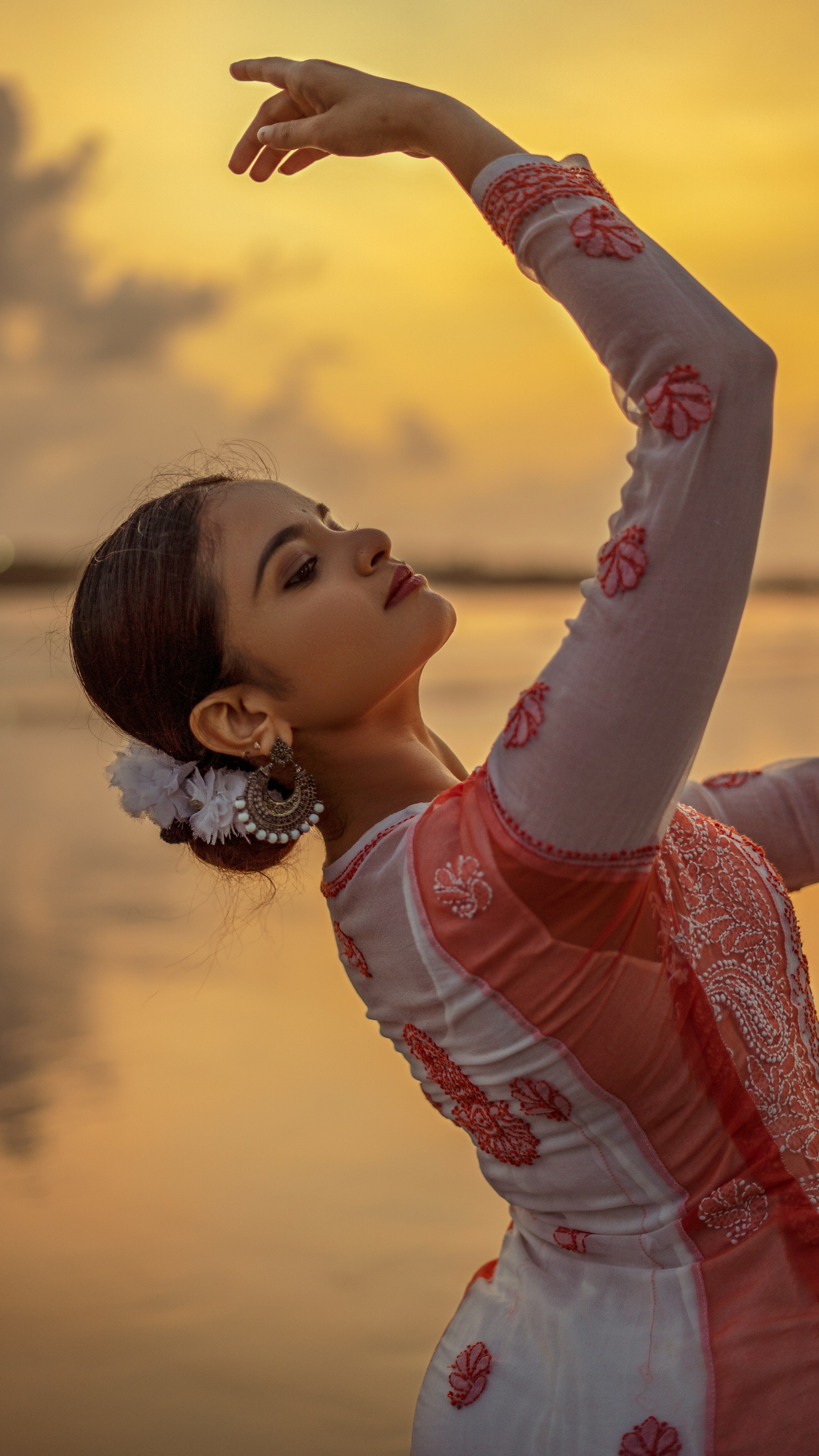 A woman in an elegant dance pose by a sunset-lit waterfront. Capturing beauty and movement.