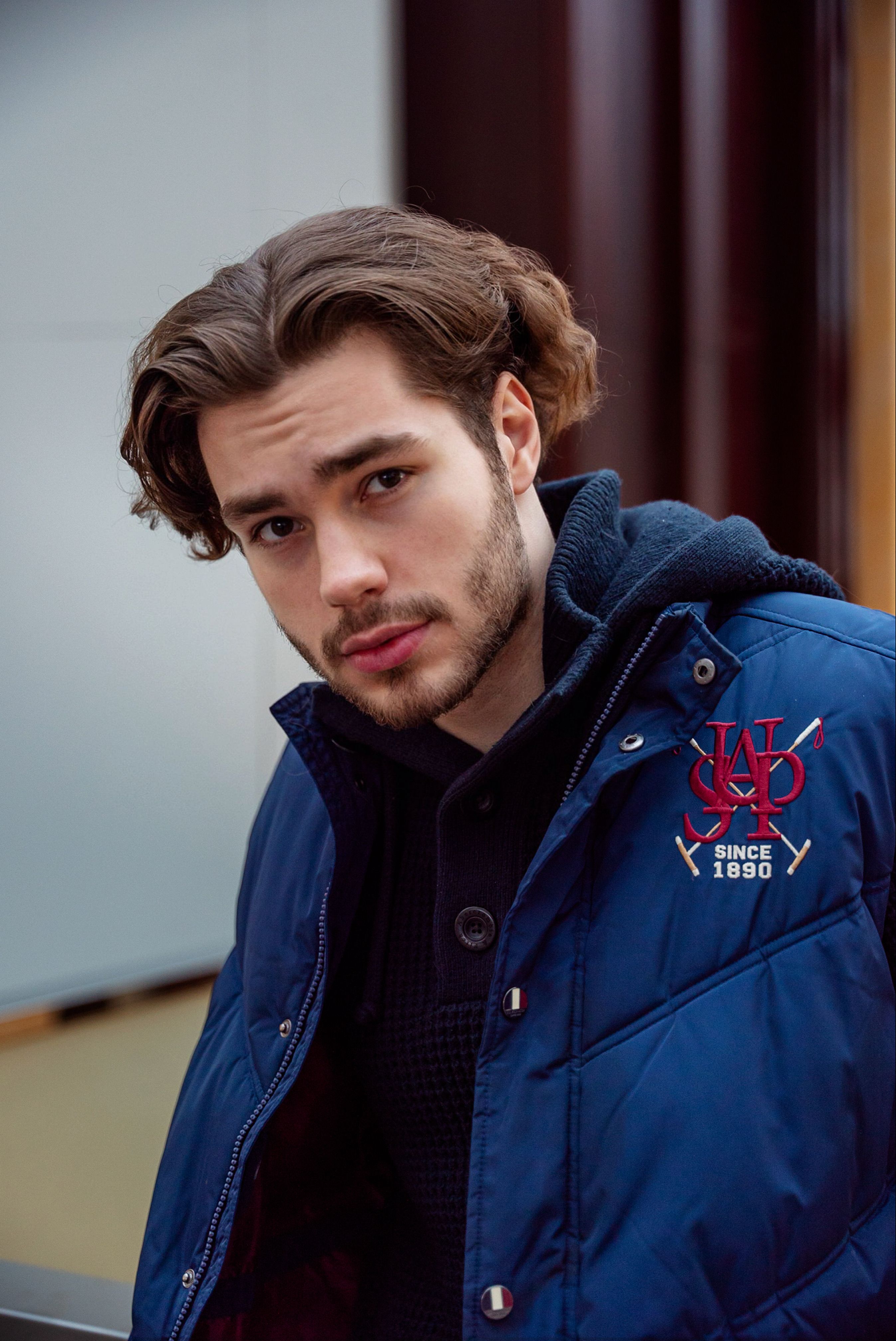 Portrait of a fashionable young man with stubble in a blue jacket and warm layers.