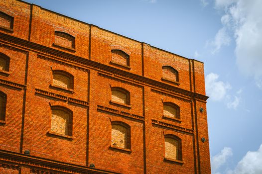 Low angle view of a historic red brick building in Łódź, Poland against a blue sky.