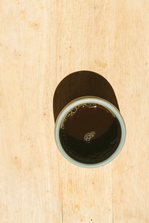 Free Aerial shot of a coffee cup casting a shadow on a wooden table, highlighting texture. Stock Photo