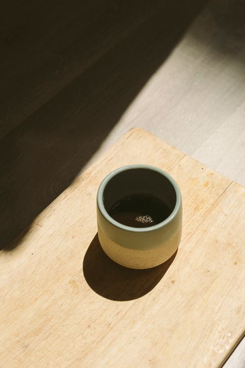 Free Stylish ceramic cup of coffee casting a shadow on a wooden tray, highlighting minimalist design. Stock Photo