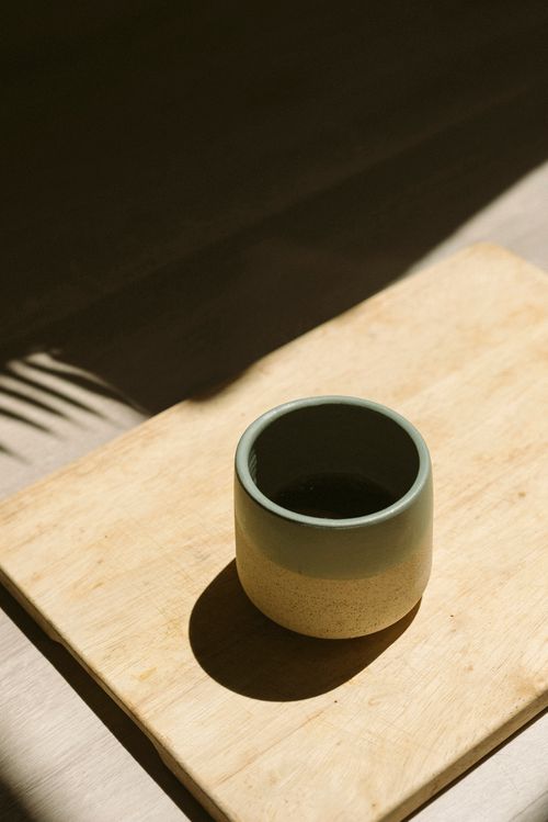 Free A minimalist ceramic coffee cup placed on a wooden board, elegantly lit by sunlight. Stock Photo