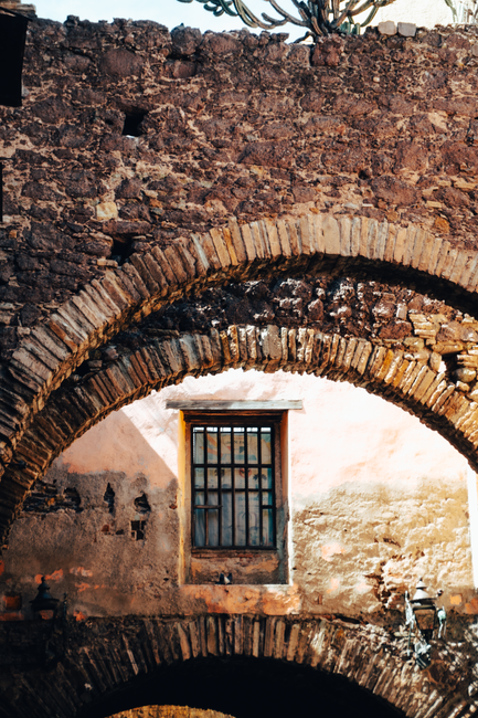Old stone arches with a rustic window, showcasing weathered textures and historic architecture.
