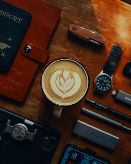 Free Top view of cappuccino with latte art surrounded by travel essentials on a wooden table. Stock Photo