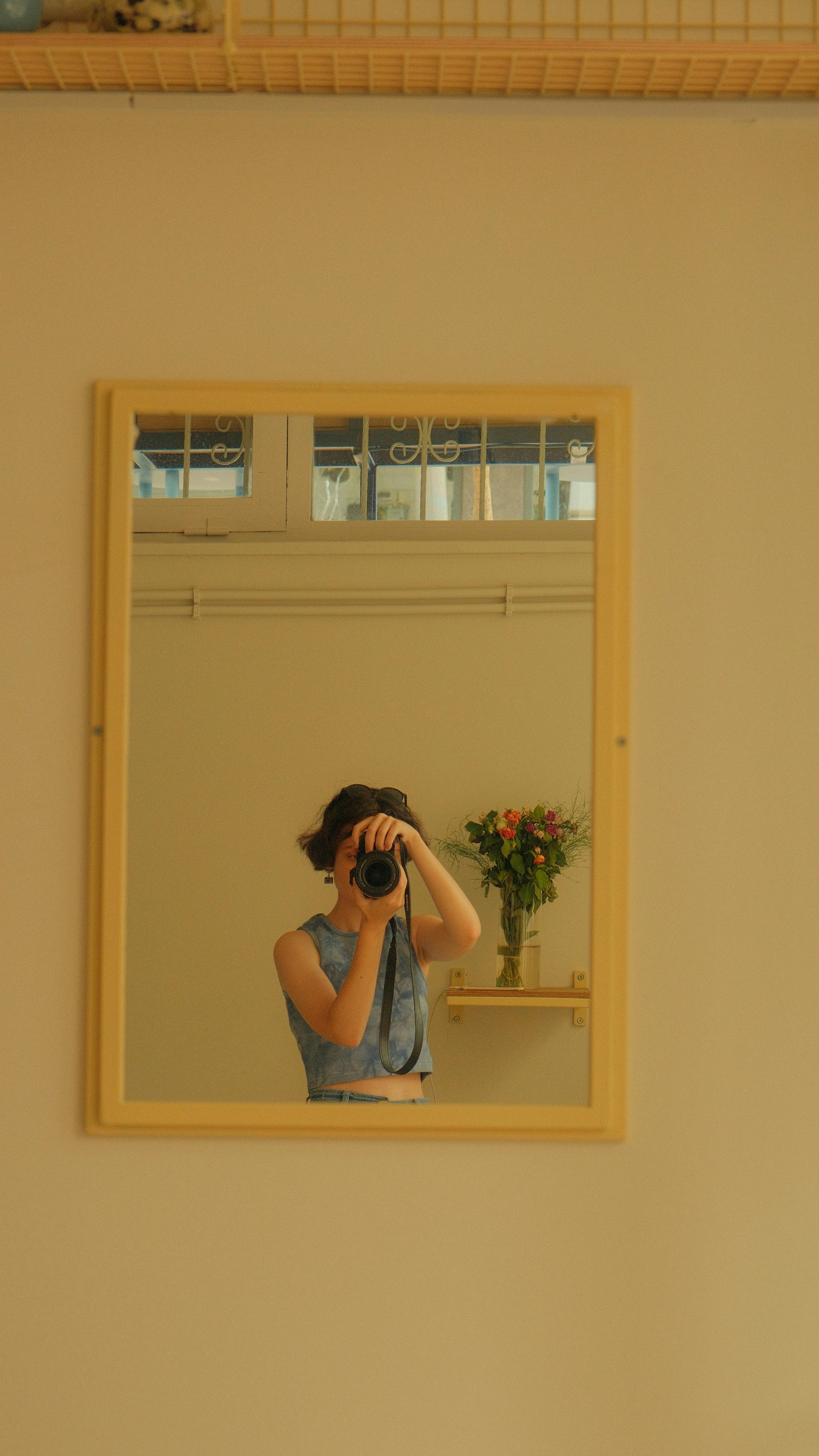 A woman holding a camera takes a photo in a mirror, capturing a cozy indoor setting.