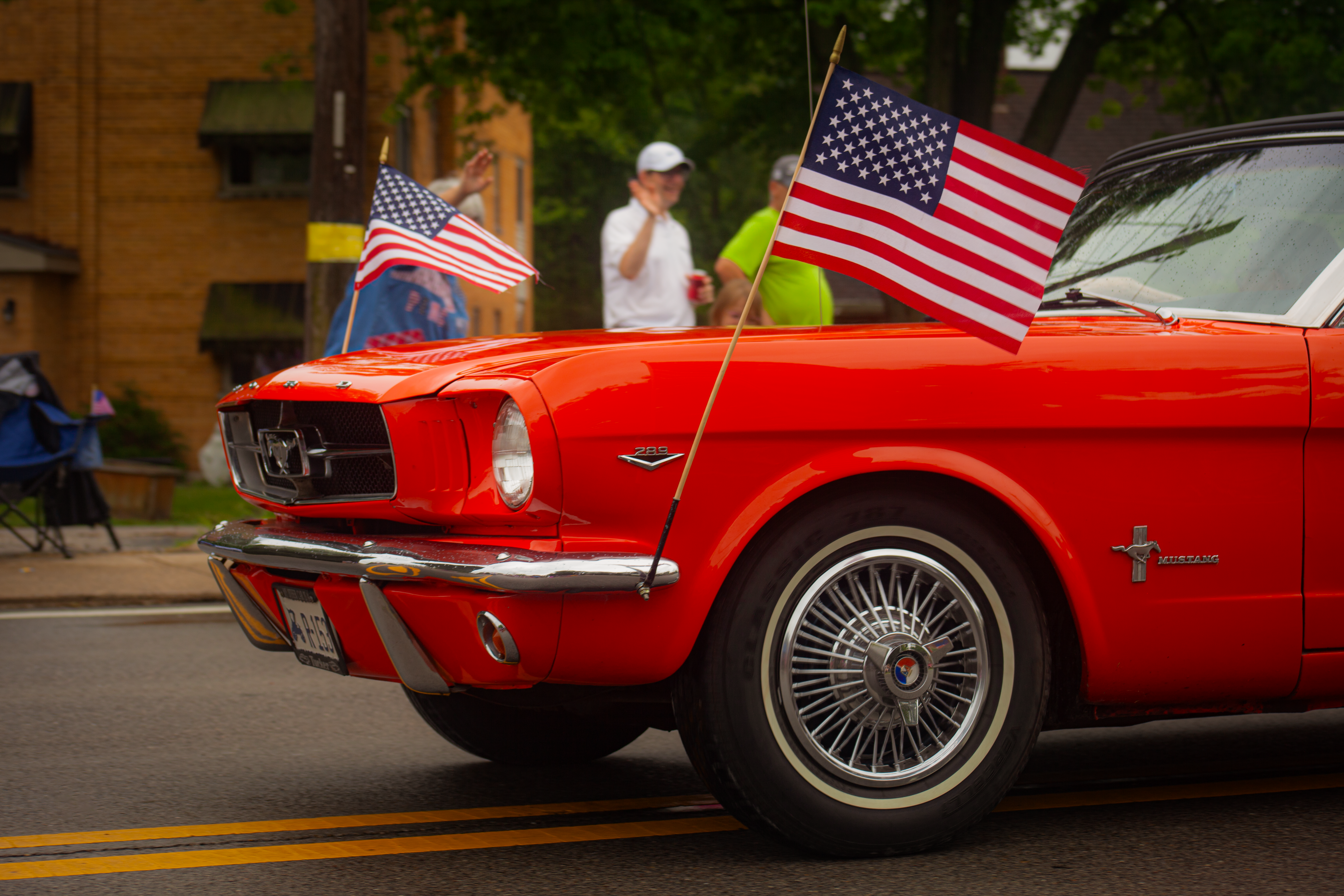 Classic red Ford Mustang adorned with American flags on a city street, celebrating patriotism.
