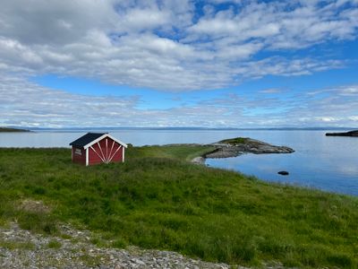 Gift card artwork: a red cabin beside a tranquil sea — photo by Petra Nesti on Pexels