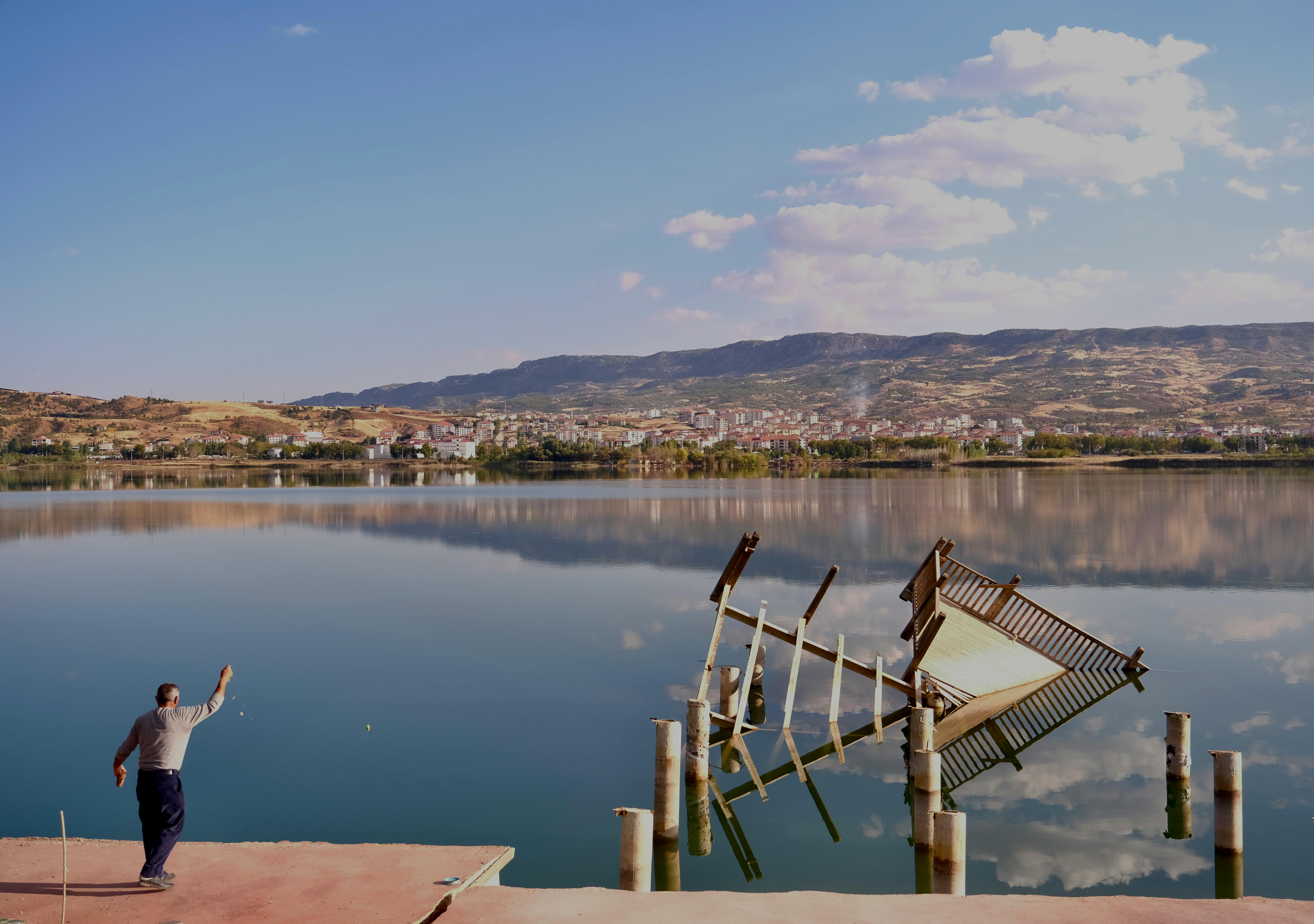 A serene lake view in Adıyaman with a man and a collapsed pier reflecting in the water.