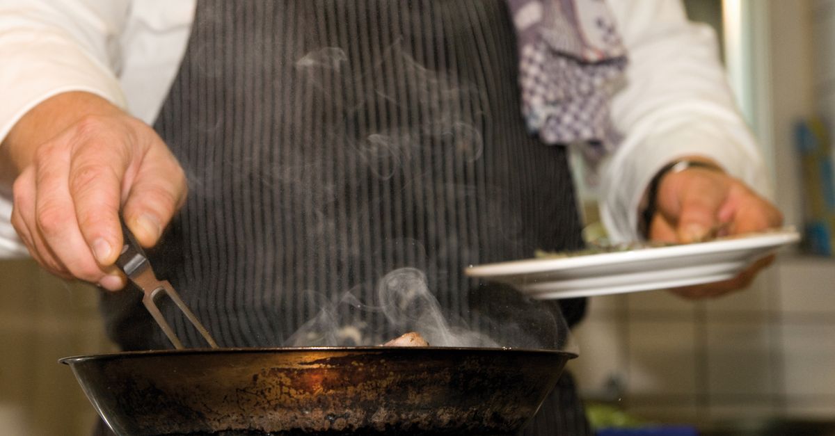 close-up of a chef squeezing tomato paste from a tube into a sizzling pan