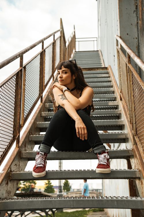 Free Portrait of a young woman sitting thoughtfully on an outdoor staircase. Urban setting and casual style. Stock Photo