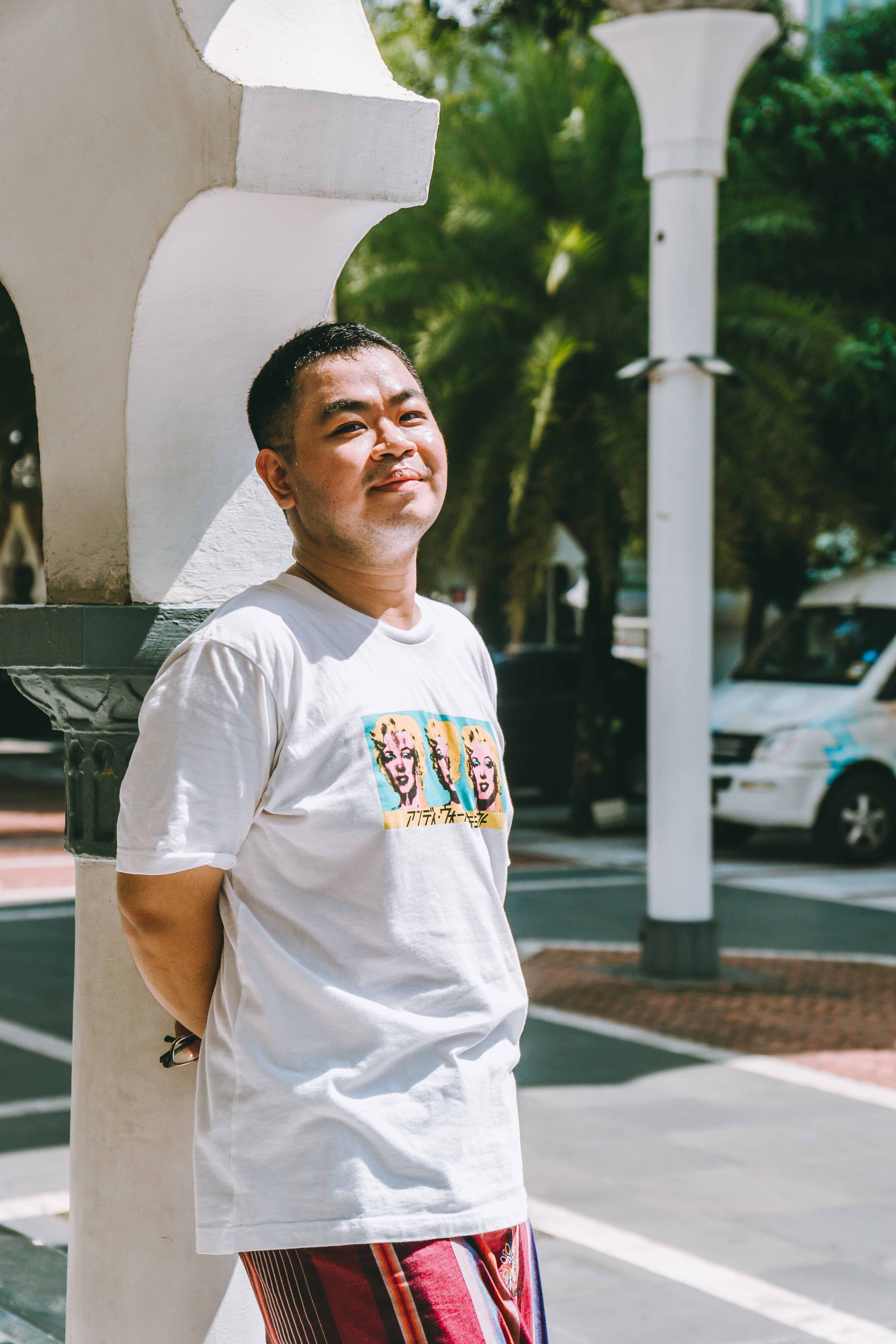 Man posing casually in a Kuala Lumpur street under bright sunlight.