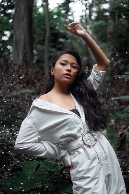 Stylish woman posing in a white jumpsuit amidst lush greenery in Bandung, Indonesia.