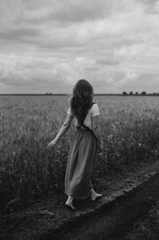 A woman walks barefoot through a rural wheat field in a carefree manner, embracing nature.