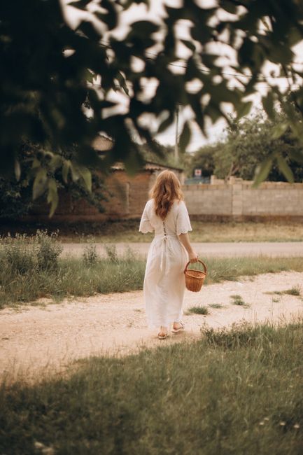 A serene scene of a woman in a white dress walking on a path carrying a basket.