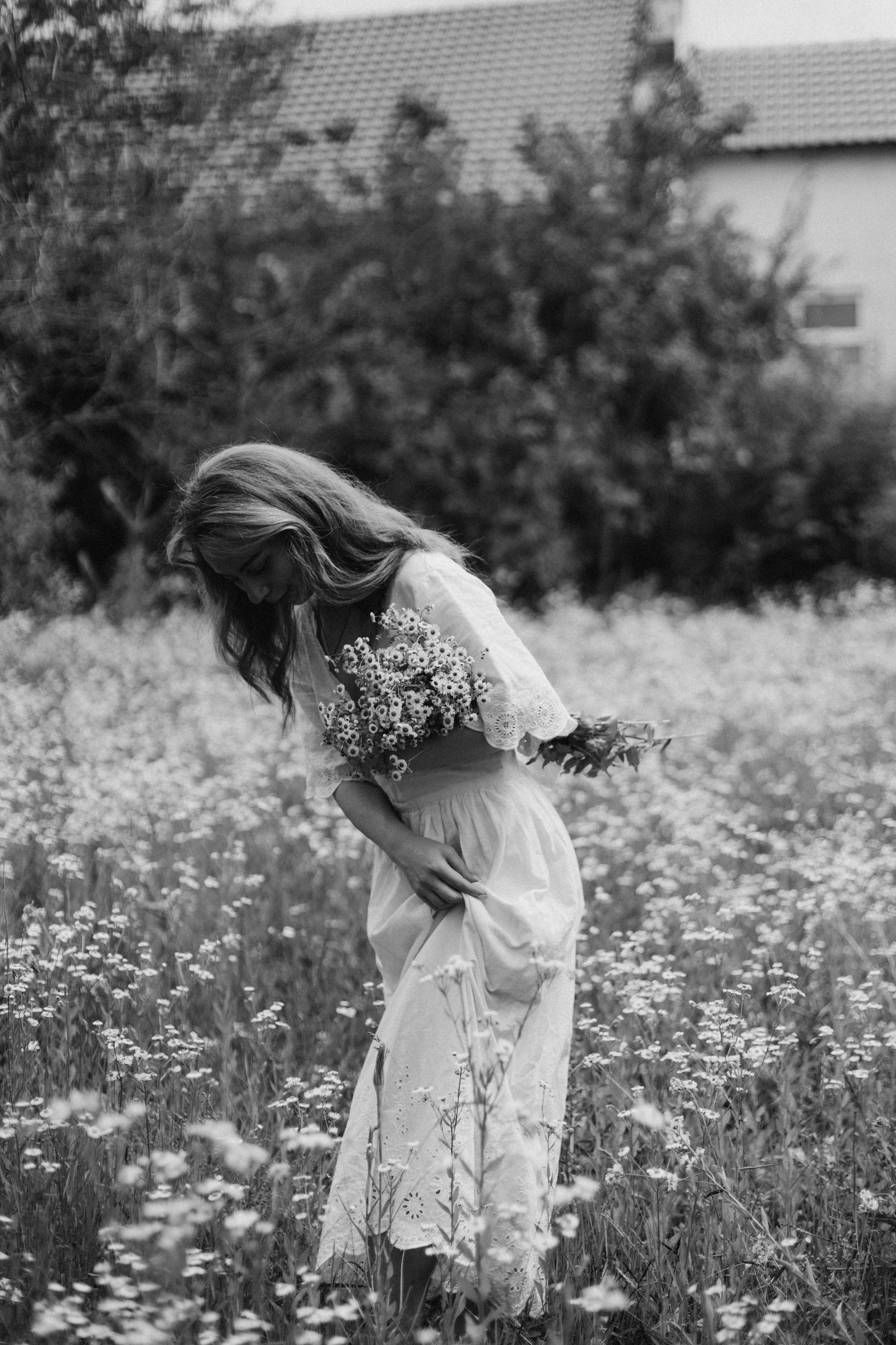 Black and white photo of a woman in a meadow holding flowers, evoking a rustic summer vibe.