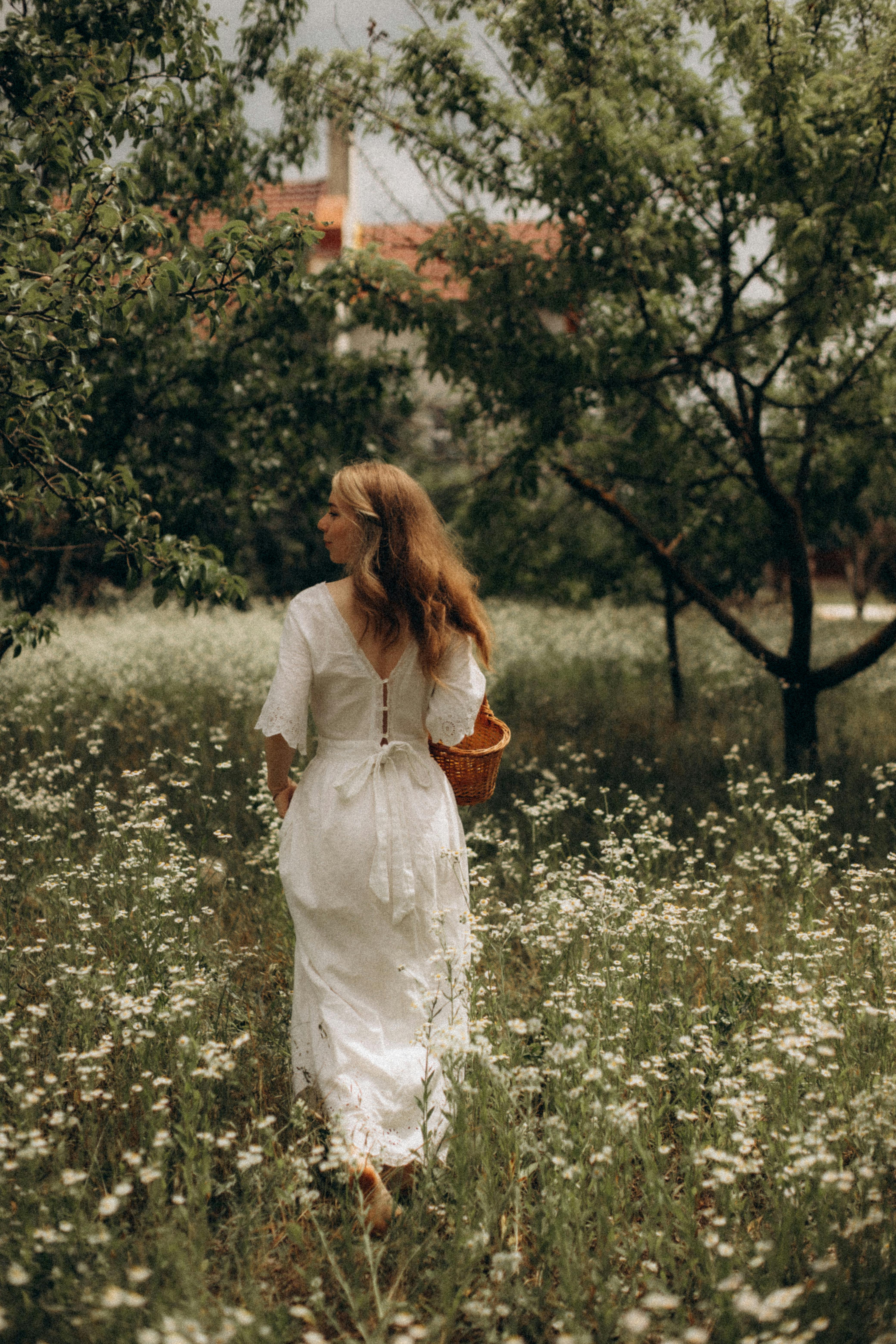 woman in white dress walking with wicker basket on meadow