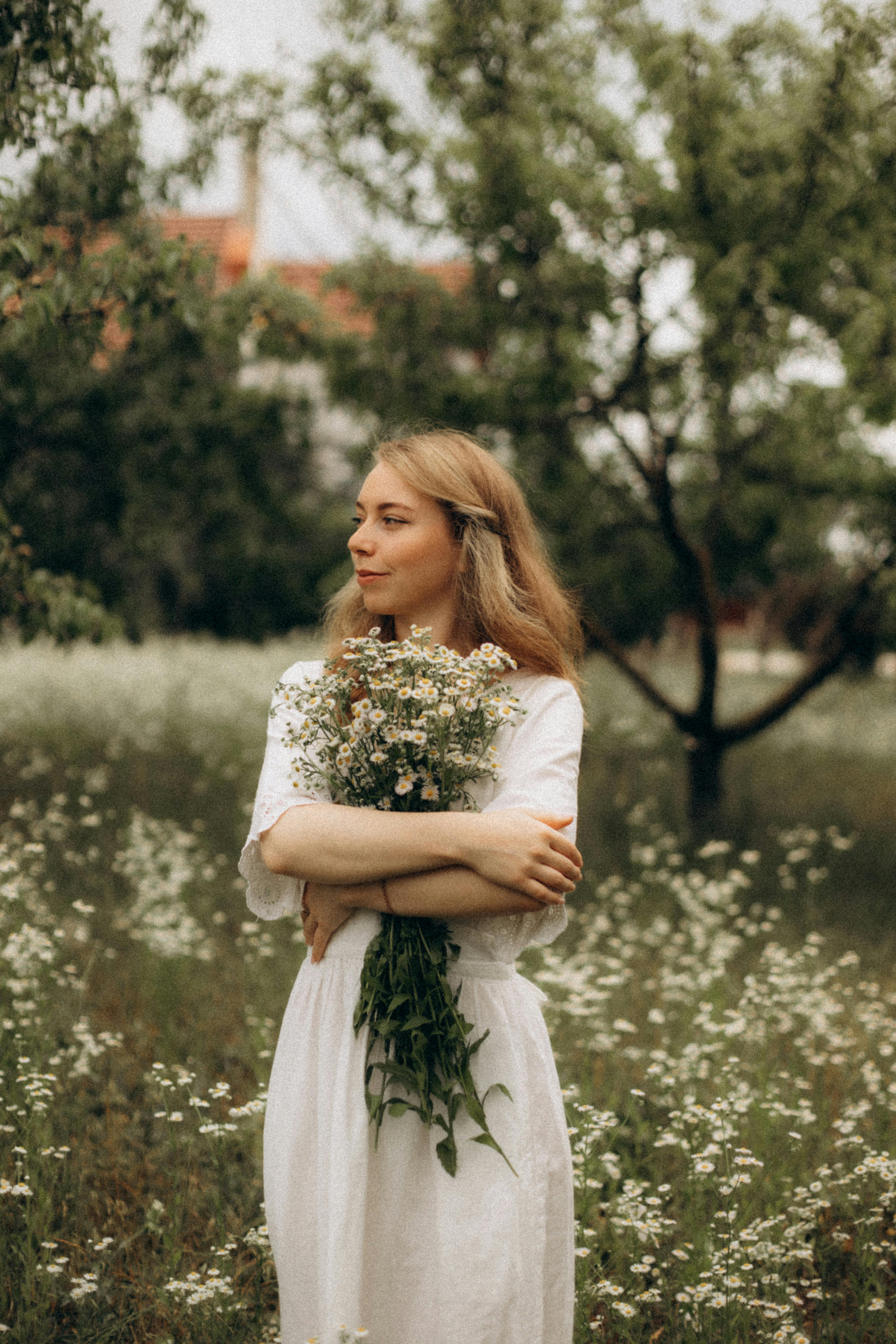 A serene woman in a white dress holds a bouquet of wildflowers in a lush meadow.