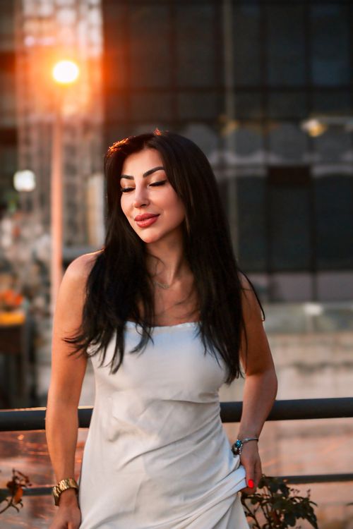 Free Stylish woman in a white dress enjoys a sunset on a rooftop in the city. Stock Photo