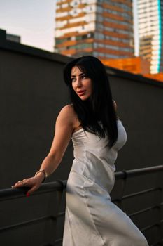 Stylish woman in white dress posing on a city rooftop, captured at sunset.