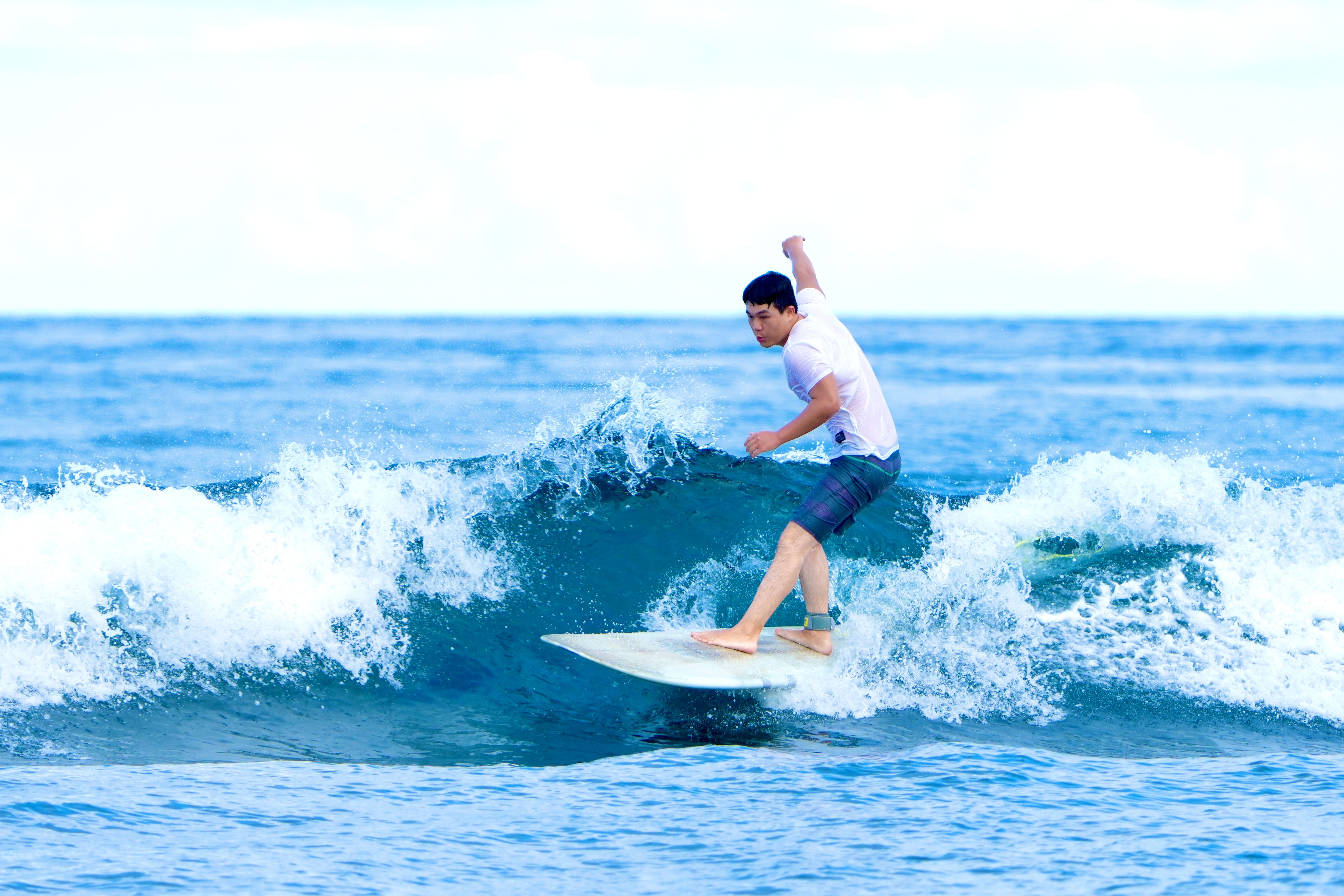 Adult man skillfully riding a wave with a white surfboard in the ocean, showcasing surfing action.