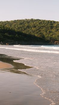 Peaceful beach scene with rolling waves, sandy shores, and lush green hills.