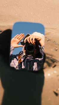 Mirror reflection of person holding camera on a sunny beach day, capturing creativity and self-portrait art.