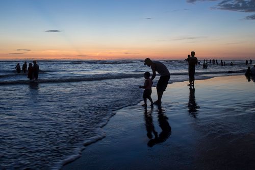 Free A tranquil beach scene featuring silhouettes of people enjoying the ocean at sunset. Stock Photo