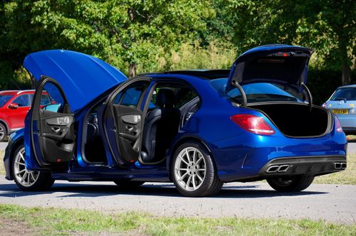 Free A sleek blue Mercedes-Benz AMG C63 with open doors in an outdoor parking area under sunlight. Stock Photo