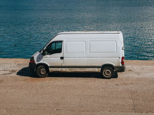 Free A white van parked next to a serene blue sea on a sunny day. Stock Photo