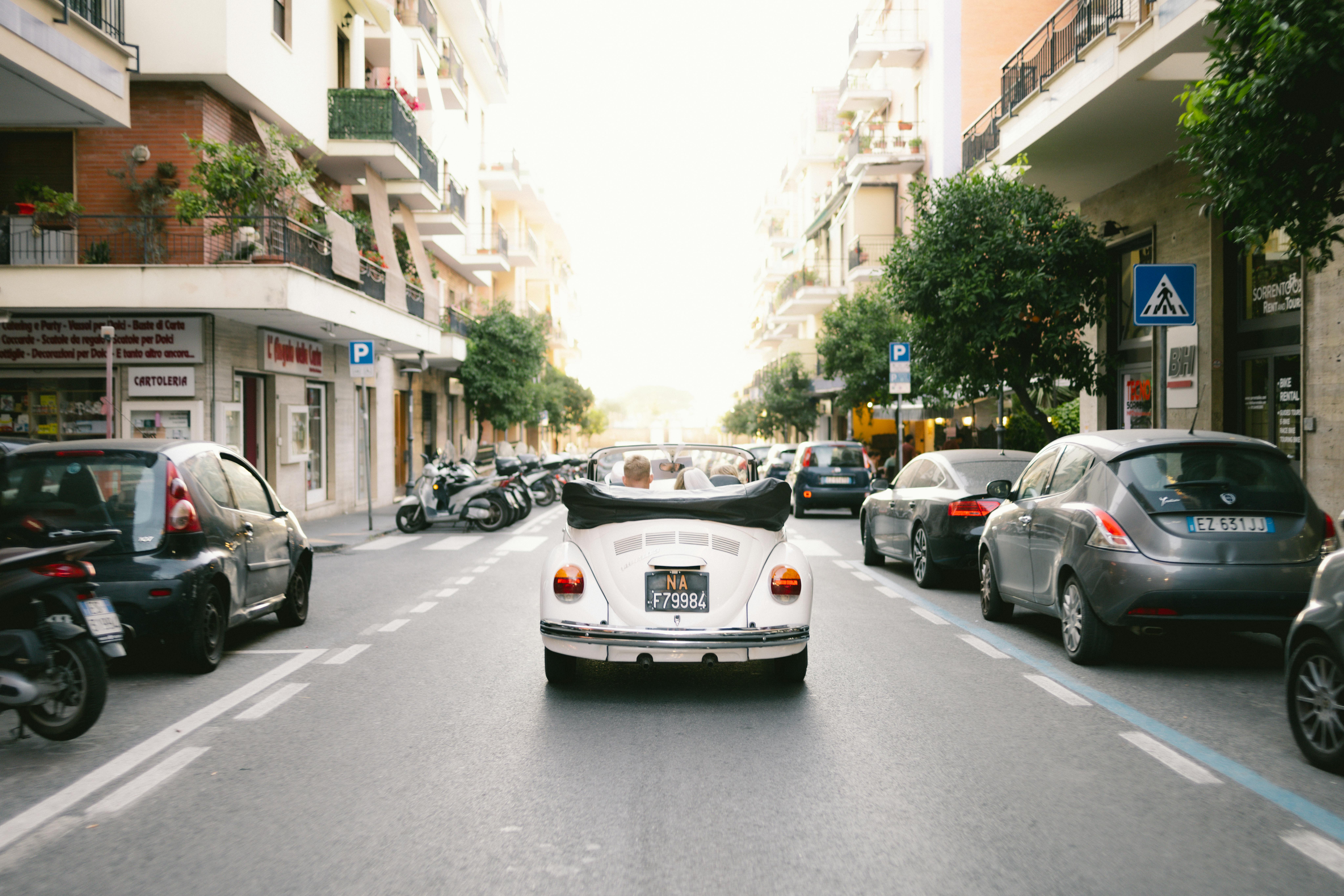 White convertible car cruising through urban streets of Sorrento, Italy, capturing summer vibes.