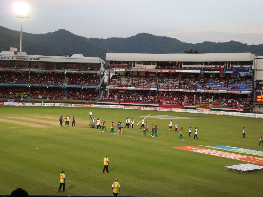 A packed cricket stadium crowd watching a live match from the stands on a sunny day.