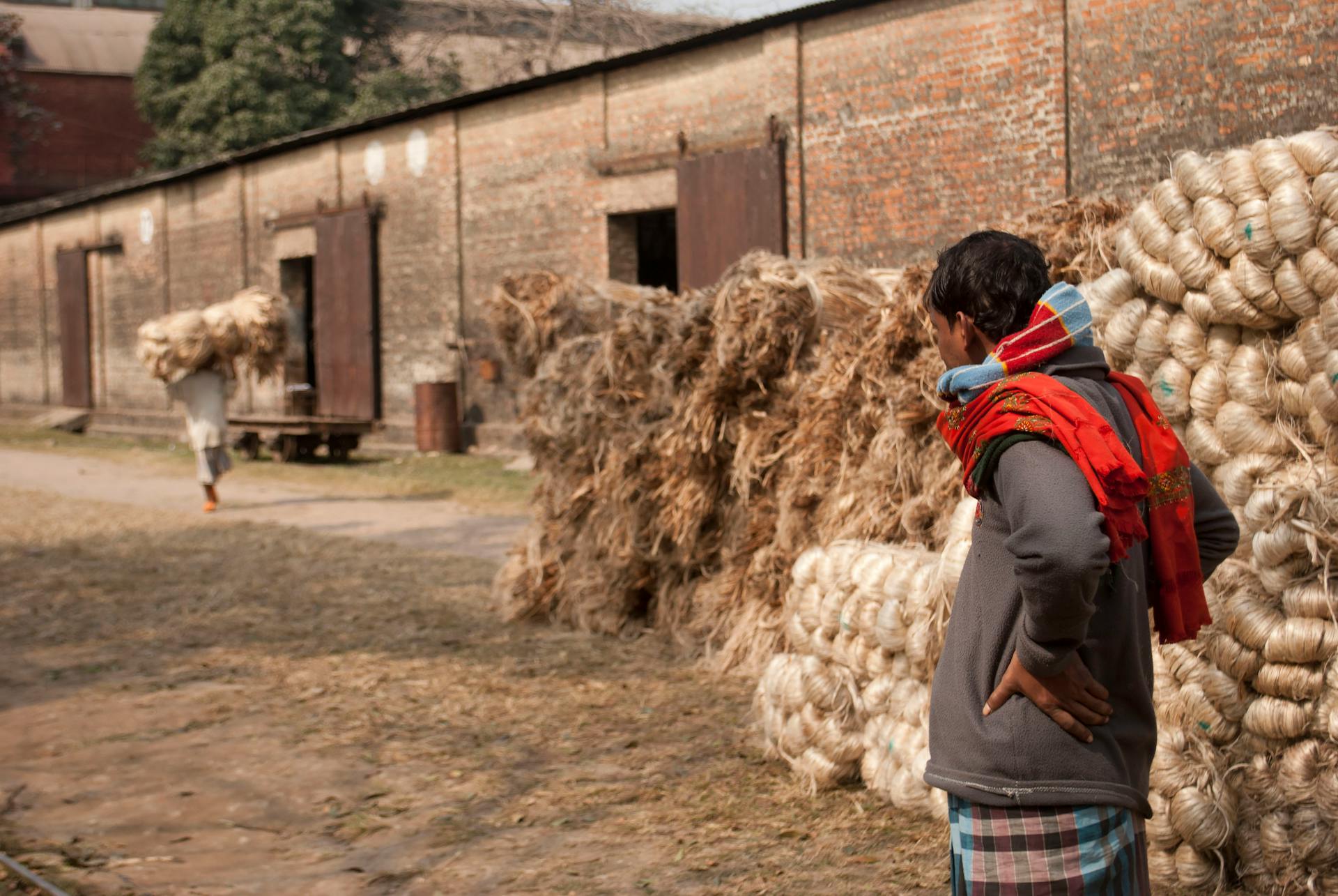 A rural worker stands outside a warehouse with hay, symbolizing agricultural labor.