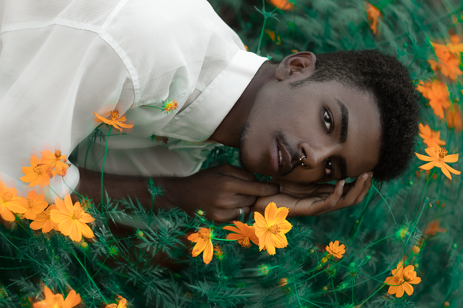 A young man poses in a vibrant field of orange flowers, creating a serene, fashionable image.