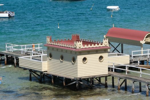 Victorian-style bathhouse on a wooden pier over clear blue sea, perfect for leisure and travel themes.