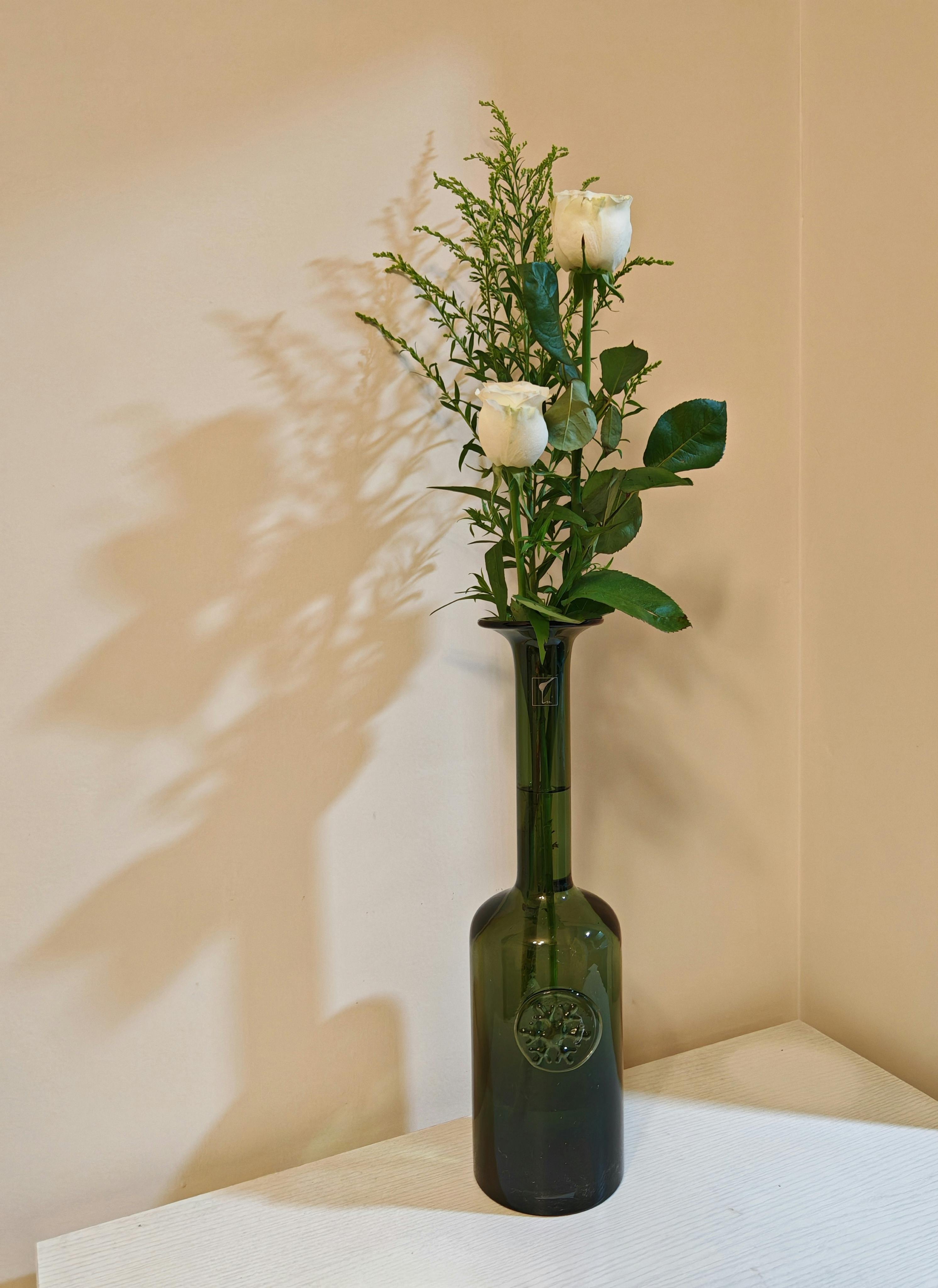 Free Elegant arrangement of white roses in a green glass vase casting a delicate shadow. Stock Photo