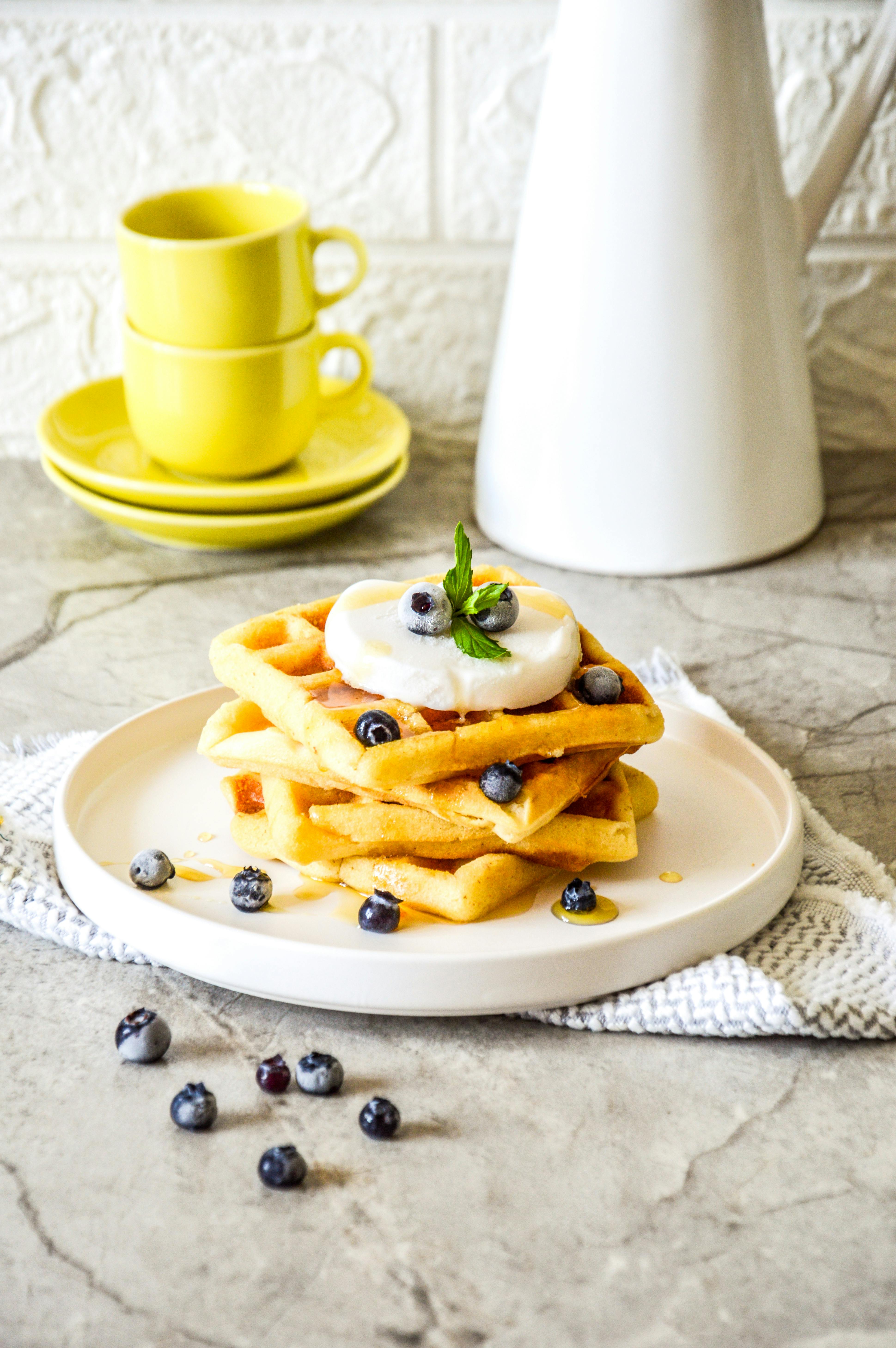 Stack of homemade waffles topped with blueberries and cream, perfect for a sweet breakfast.