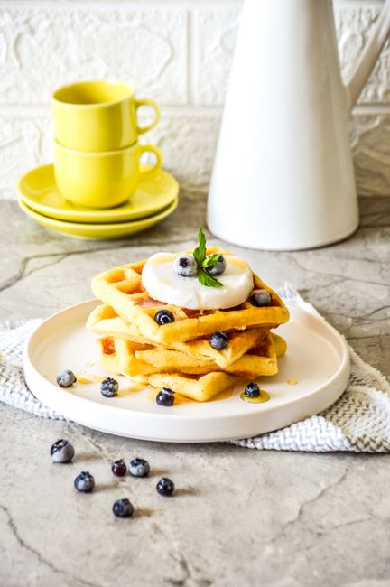 Stack of homemade waffles topped with blueberries and cream, perfect for a sweet breakfast.