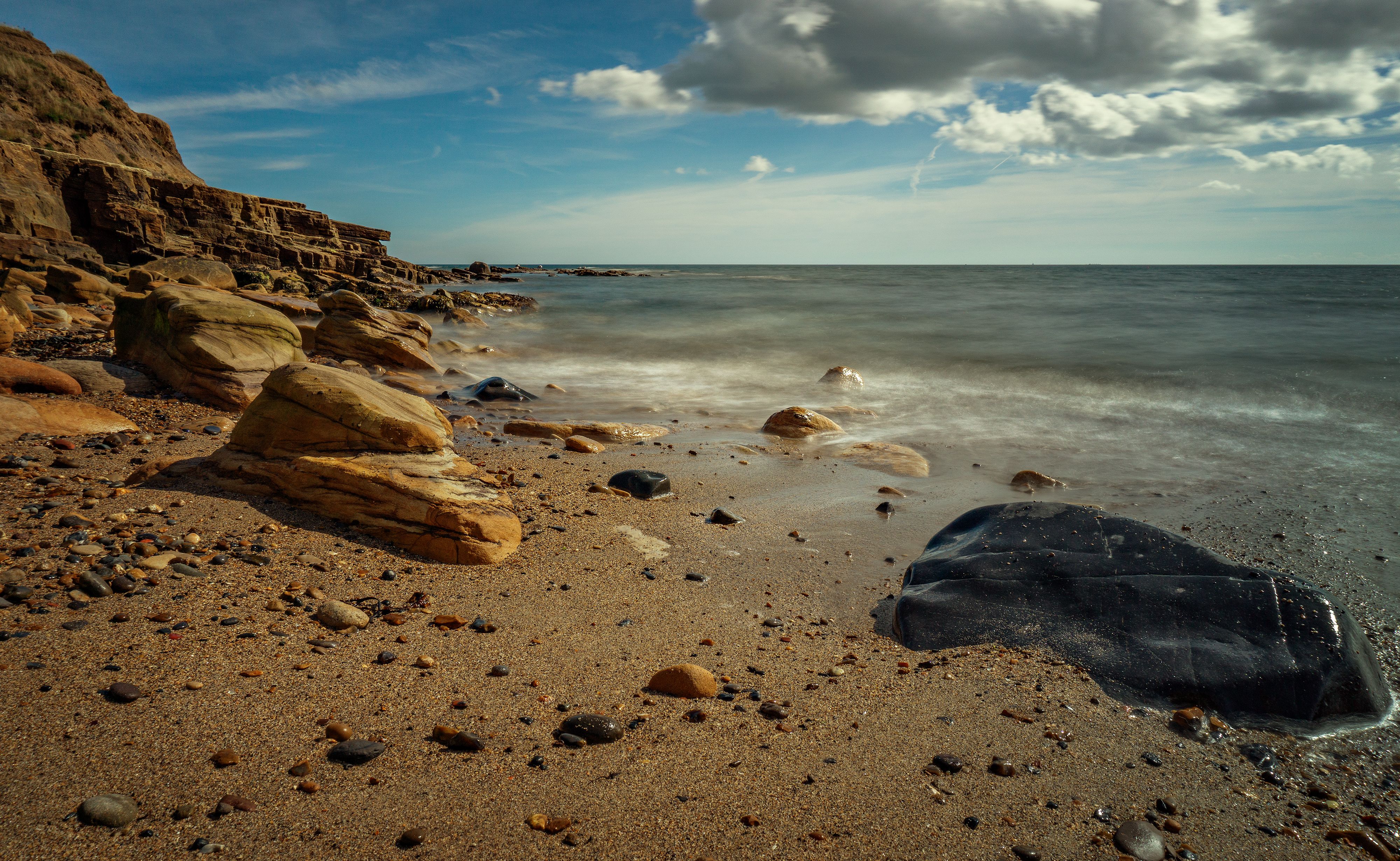 A beach with rocks and a cloudy sky · Free Stock Photo