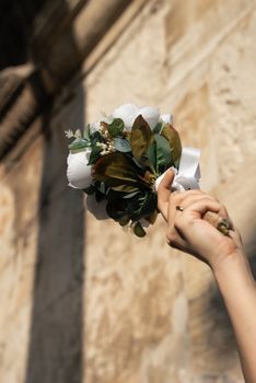 A hand elegantly holds a bouquet of white flowers against a textured urban wall backdrop.